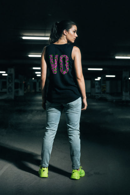 Person wearing a black sleeveless shirt with 'V0' design, light blue jeans, and green shoes in a dark indoor setting.